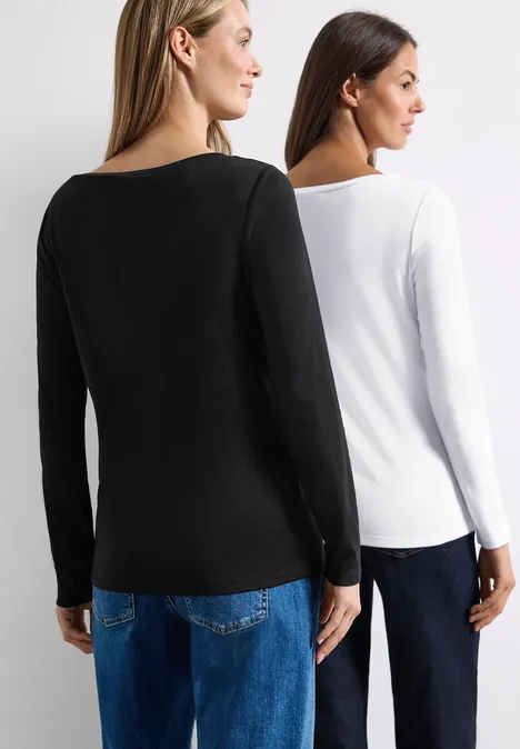 Zwei Frauen stehen Rücken an Rücken, tragen schlichte Langarmshirts in Schwarz und Weiß sowie blaue Jeans.