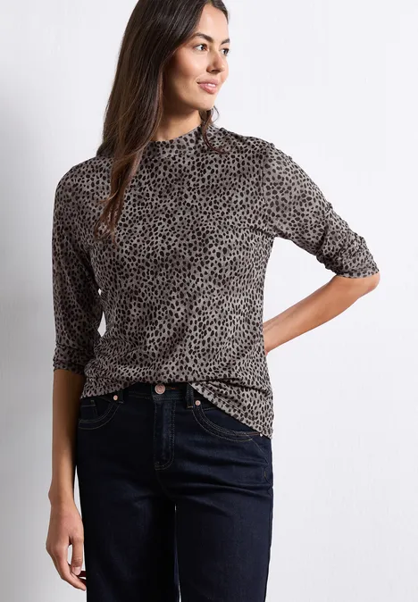 Vrouw met stippencoltrui en donkere jeans poseert voor een witte achtergrond.