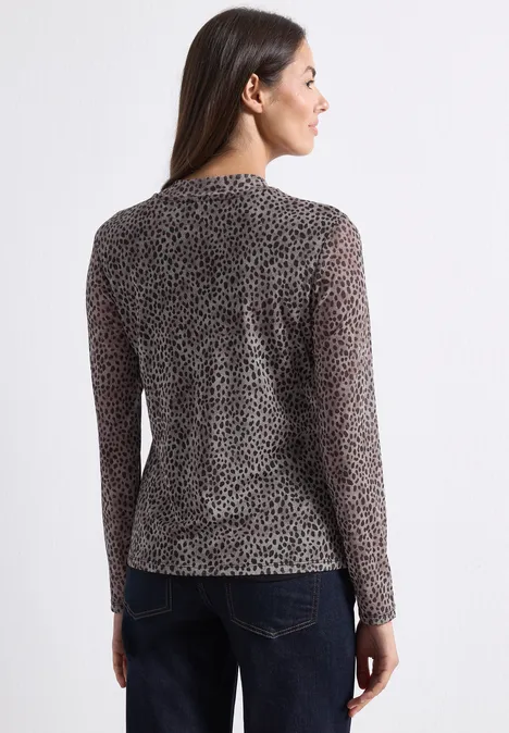 Vrouw van achteren in zwarte, transparante, lange mouwen luipaardtop en blauwe jeans, hoofd opzij gedraaid.