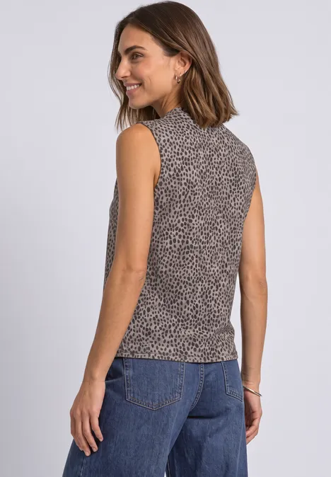 Femme de dos portant un top sans manches à motifs et un jean, souriante.