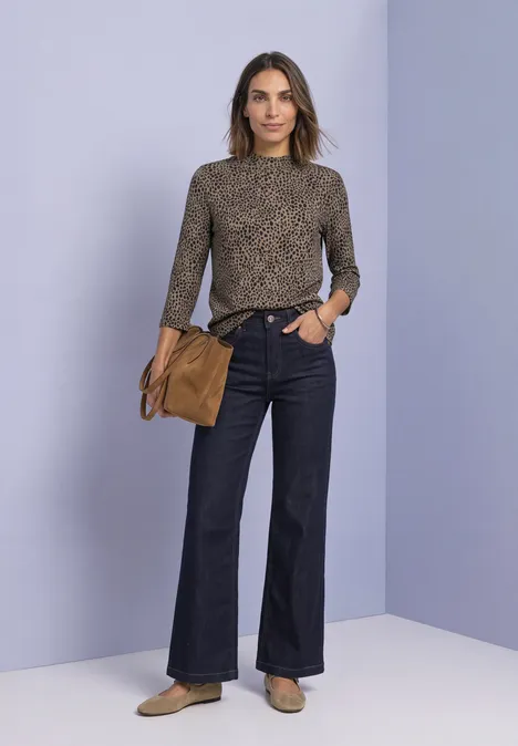 3/4-Arm Shirt mit Turtle Neck und Print Black Frau in gemustertem Oberteil, weitem Jeans, mit Tasche vor lilafarbenem Hintergrund.