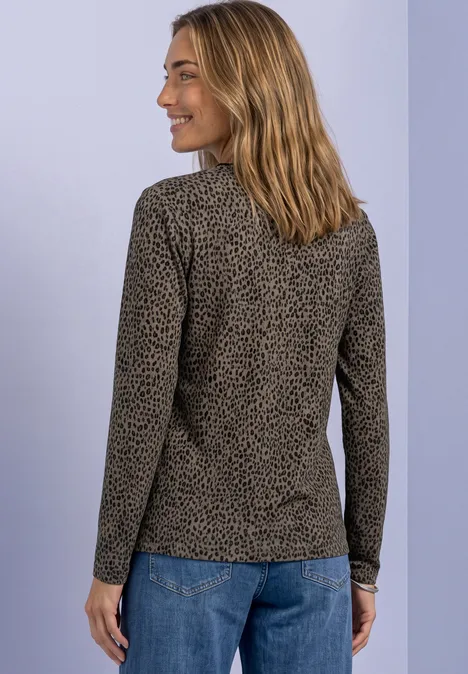 Femme de dos, légèrement de profil, portant un tee-shirt manches longues à motifs et un jean, fond clair.