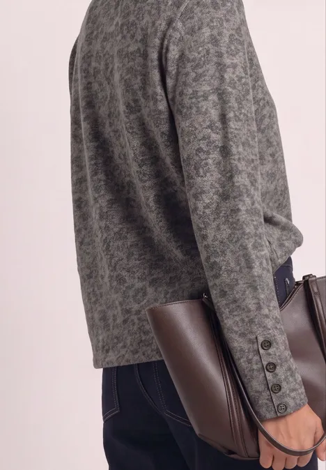 Personne portant un blazer gris à motif, jean foncé, tenant un sac en cuir marron.