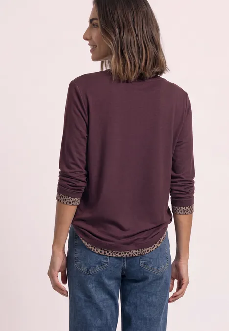 T-shirt à manches longues avec effet color block et imprimé rustic rouge Rückenansicht einer Frau in bordeauxroter, langärmliger Bluse mit gemusterter Innenmanschette und blauen Jeans.