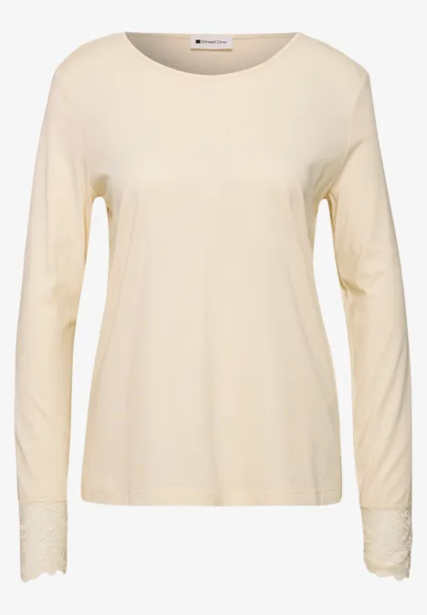 Beiges Langarmshirt aus weichem Stoff mit rundem Halsausschnitt und feiner Spitzenverzierung an den Ärmeln.