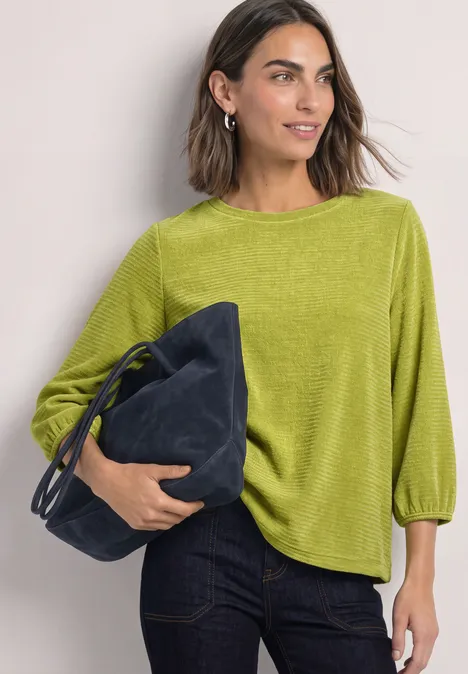 Frau in grünem Oberteil und Jeans, die eine dunkelblaue Tasche hält.