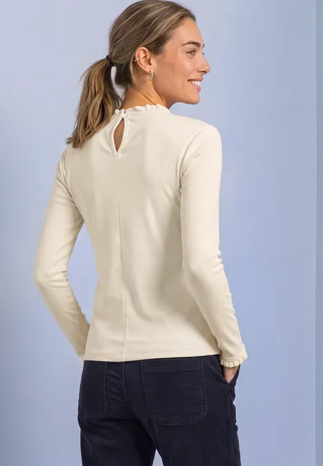 Langarm Shirt mit Rundhals und Rüschen pure beige Eine lächelnde Frau im Profil mit hellbeigem Langarmshirt und dunklen Jeans vor hellem Hintergrund.