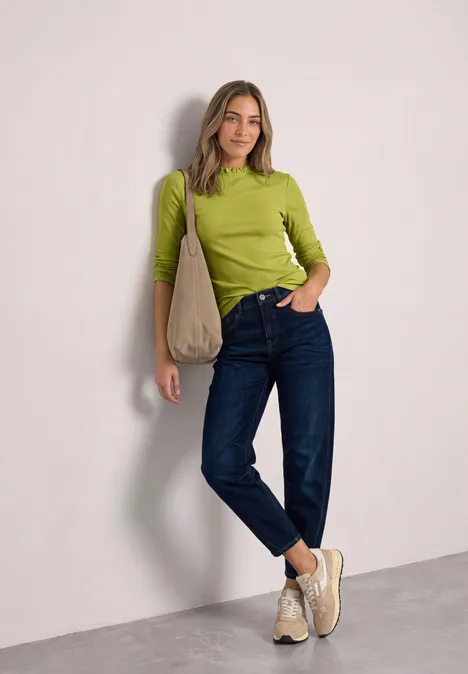 Langarm Shirt mit Rundhals und Rüschen apple lime Frau in grünem Oberteil, blauer Jeans und beigen Schuhen mit lässiger Handtasche an der Schulter.