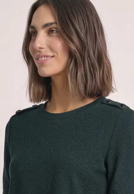 Shirt met lange mouwen, structuur en knopen stormy green Een glimlachende vrouw met bruin haar draagt een donkergroene, gestructureerde trui met knopen op de schouders.