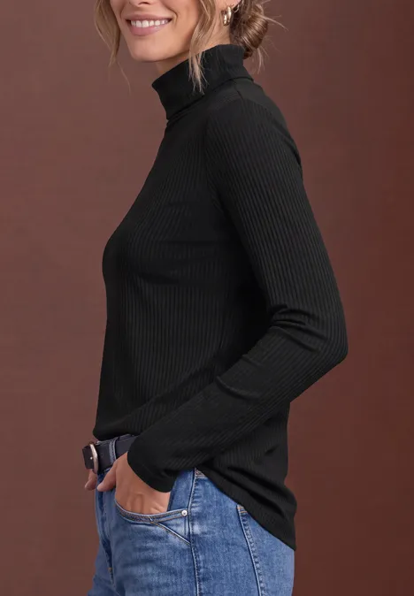 Basic coltrui Black Frau im Profil in schwarzem Rollkragenpullover und blauen Jeans vor braunem Hintergrund.