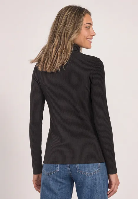 Frau mit dunkelgrauem Rollkragenpullover und Jeans, im Profil stehend.