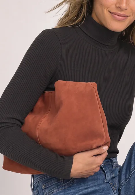 Eine Frau in schwarzem Rollkragenpullover und Jeans hält eine braune Wildledertasche.