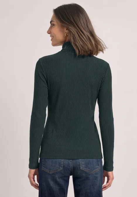 Basic shirt met col stormy green Achteraanzicht van een vrouw in donkergroene coltrui en blauwe spijkerbroek tegen een lichte achtergrond.