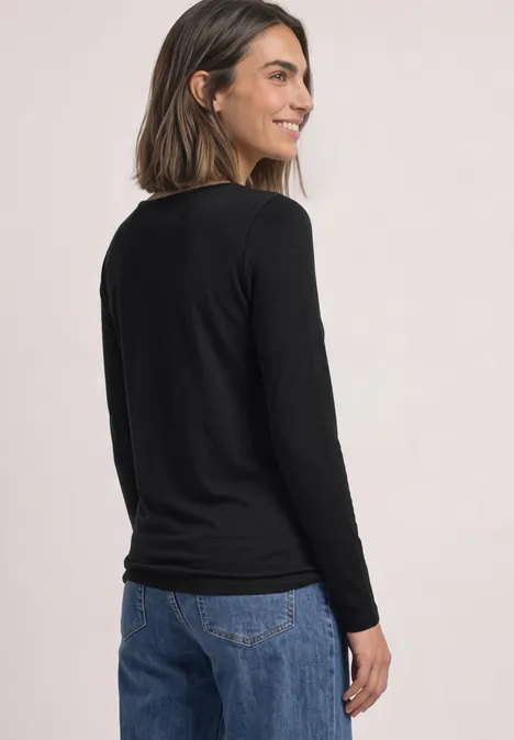 Junge Frau im Profil von hinten, trägt schwarzen Langarmshirt und Jeans, lächelt.