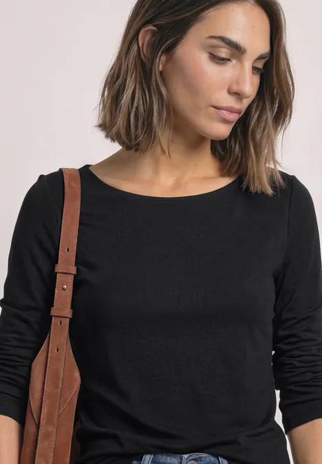 Eine Frau mit brauner Schultertasche trägt ein schlichtes schwarzes Langarmshirt.