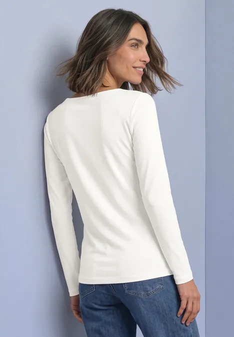 Vrouw in wit shirt met lange mouwen en jeans, van achteren licht schuin gefotografeerd.