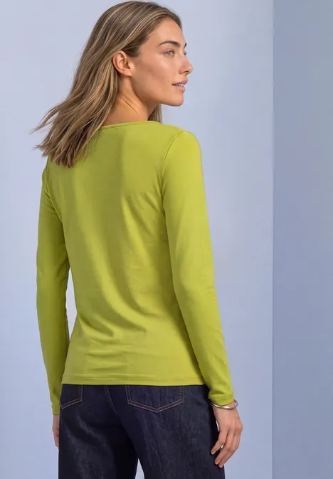 Basic Shirt met boothals apple lime Achteraanzicht van een vrouw met een lichtgroen shirt met lange mouwen en blauwe jeans voor neutrale achtergrond.