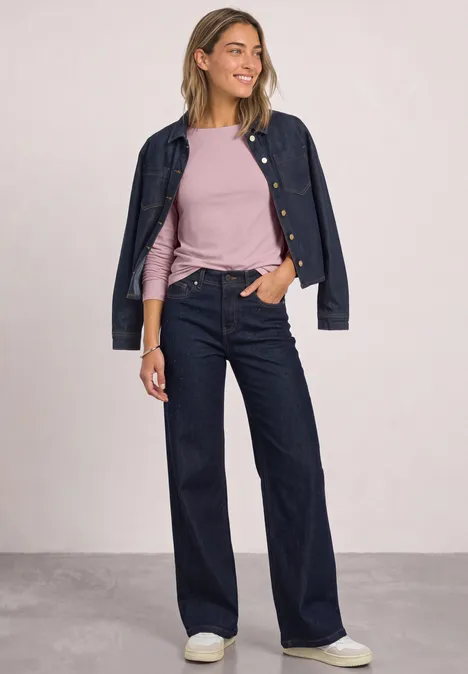 Basic shirt met boothals quiet rose Frau in dunkler Jeansjacke und -hose, rosa Shirt und weißen Sneakers, steht entspannt mit einer Hand in der Tasche.