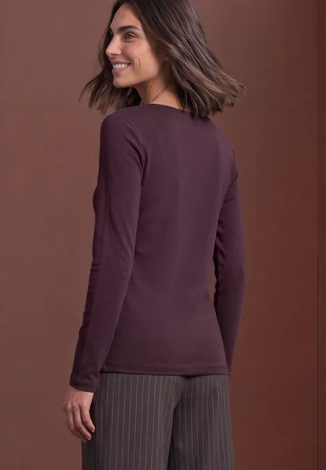 Vrouw van achteren lachend met een donkerrood langarmshirt en een gestreepte broek voor een bruine achtergrond