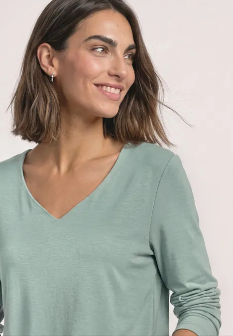 Frau mit schulterlangem Haar trägt mintgrünes Shirt mit V-Ausschnitt und lächelt seitlich.
