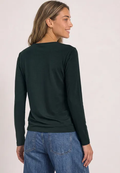 Frau von hinten in dunklem Langarmshirt und blauen Jeans, seitlich stehend.