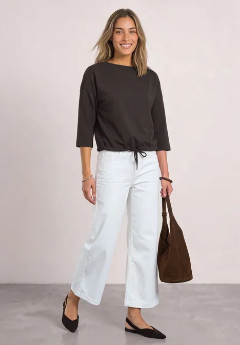 Vrouw in zwart 3/4-mouwshirt, witte wijde jeans en zwarte ballerina's, met een bruine tas.