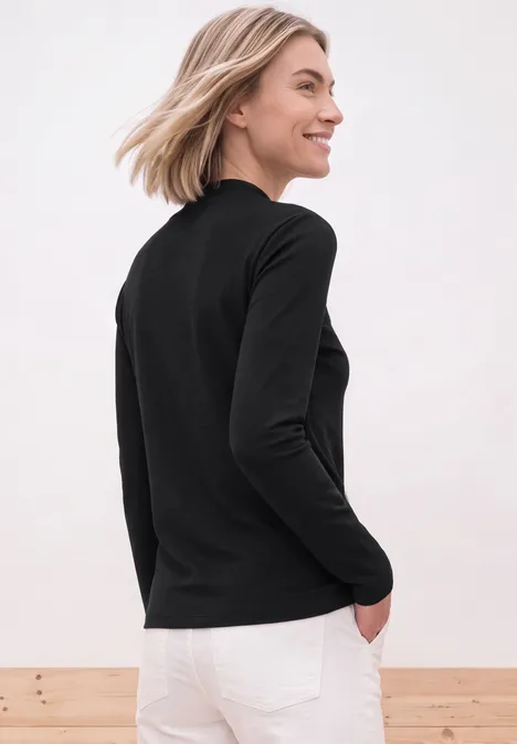 Shirt mit Turtle Neck und Schlitzdetail Black Eine Frau trägt ein schwarzes Langarmshirt und weiße Jeans, steht lächelnd seitlich.