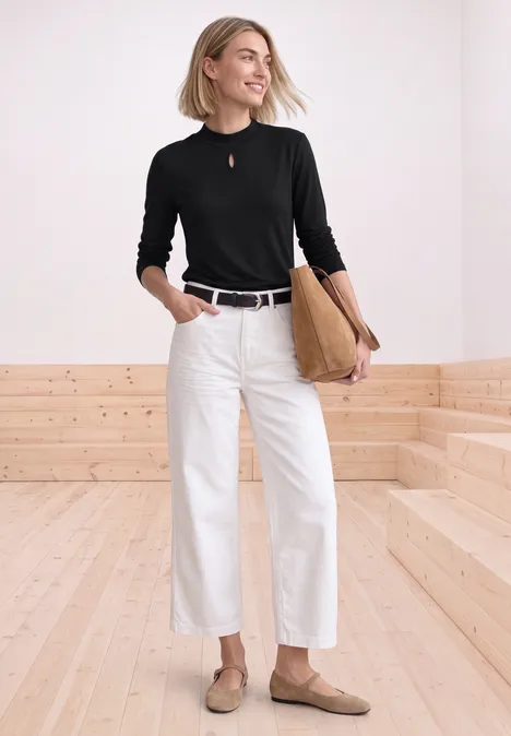 Shirt mit Turtle Neck und Schlitzdetail Black Eine Frau trägt schwarzen Pullover, weiße Hose, braune Loafers und hält eine Beuteltasche in modernem Raum.