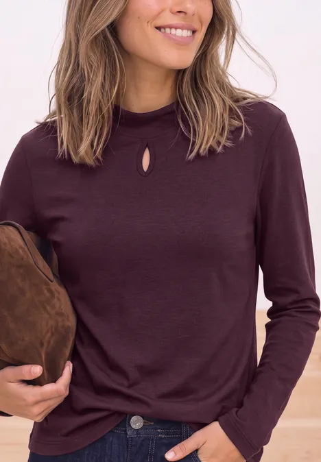 Frau im bordeauxfarbenen Langarmshirt mit kleinem Schlitz am Kragen, die eine braune Tasche hält.
