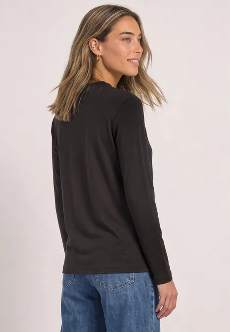 Vrouw in zijaanzicht met zwart shirt met lange mouwen en blauwe jeans, kijkt over haar schouder.
