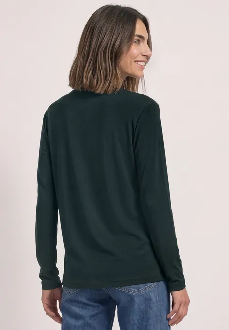 Vrouw van achteren met zwarte longsleeve en spijkerbroek, kijkt glimlachend om.