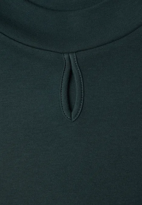 Donkergroen shirt met ronde hals en kleine druppelvormige uitsnijding net onder de kraag.