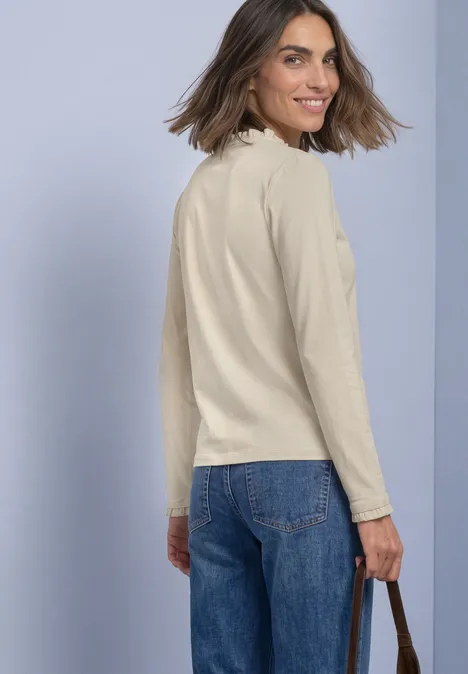Basic Shirt mit Rüschen und Cut-Out-Detail pure beige Frau in beiger Bluse und Jeans blickt lächelnd über die Schulter.