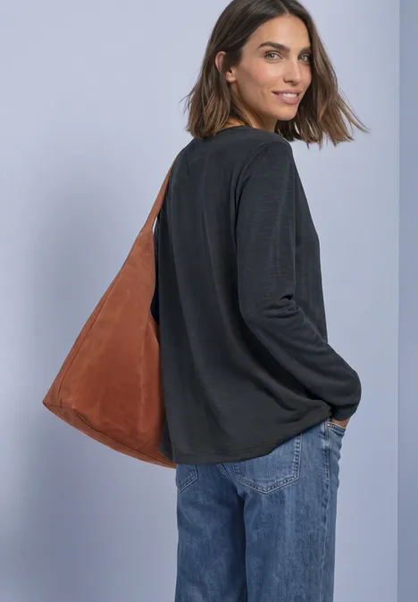 Eine Frau im schwarzen Longsleeve und blauen Jeans, schaut zurück und trägt eine braune Schultertasche.