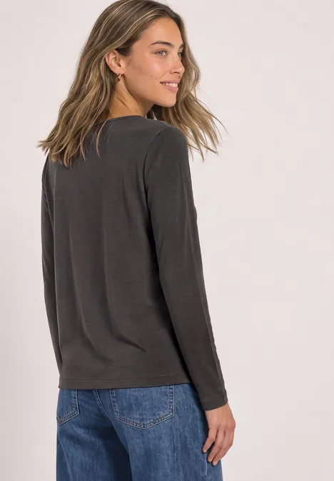 Eine Frau im dunklen Langarmshirt und Jeans, von hinten stehend und lächelnd nach rechts blickend.