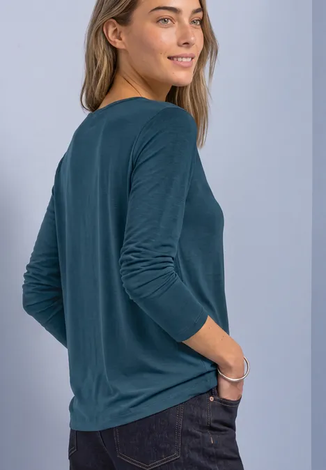 Frau von hinten in türkisfarbenem Langarmshirt, mit rechter Hand in Jeans-Tasche