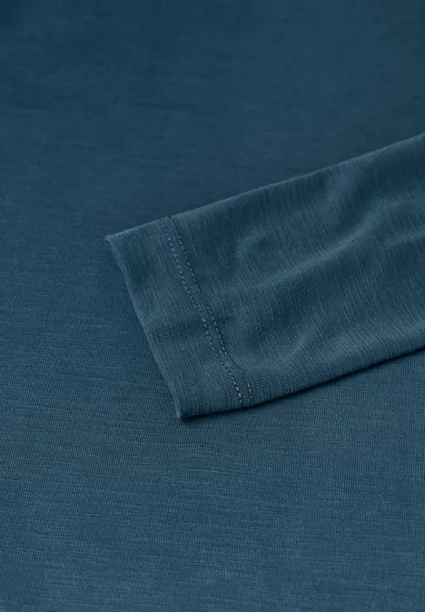 Nahaufnahme eines dunkelgrünen langärmligen Shirts mit geripptem Ärmelbündchen auf einfarbigem Untergrund.