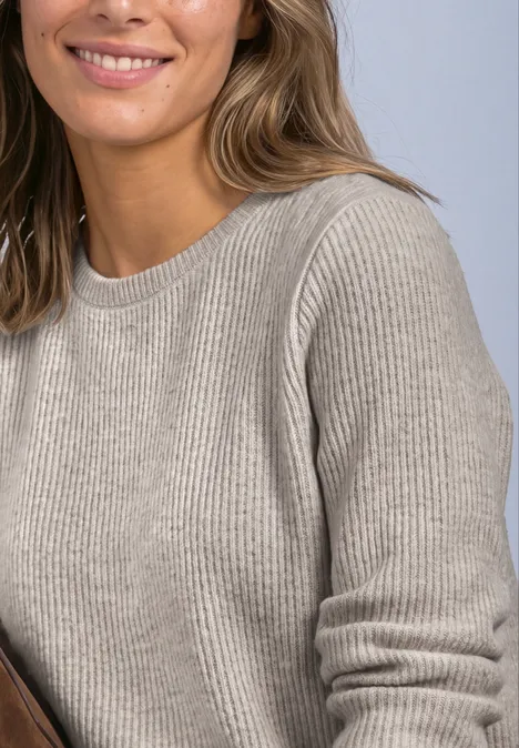 Vrouw lacht in een beige geribbelde trui, ontspannen pose.