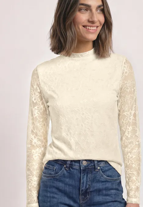 Frau trägt cremefarbige Spitzenbluse mit langen Ärmeln und eine blaue Jeans.
