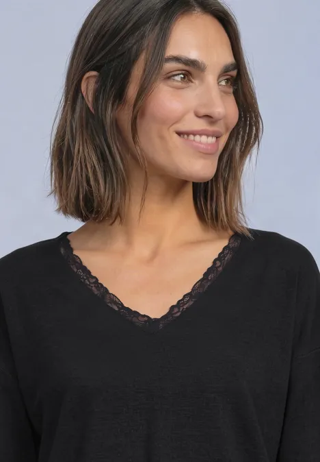 Eine lächelnde Frau mit schulterlangem braunem Haar und einem schwarzen Spitzen-V-Shirt.