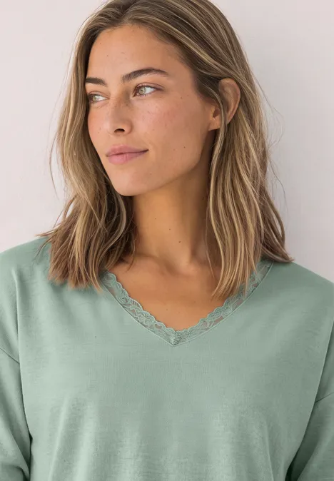 Jonge vrouw in pastelgroen V-hals T-shirt met kantrand kijkt opzij.