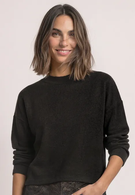 Vrouw met bruin haar in een zwarte trui, glimlachend naar de camera.