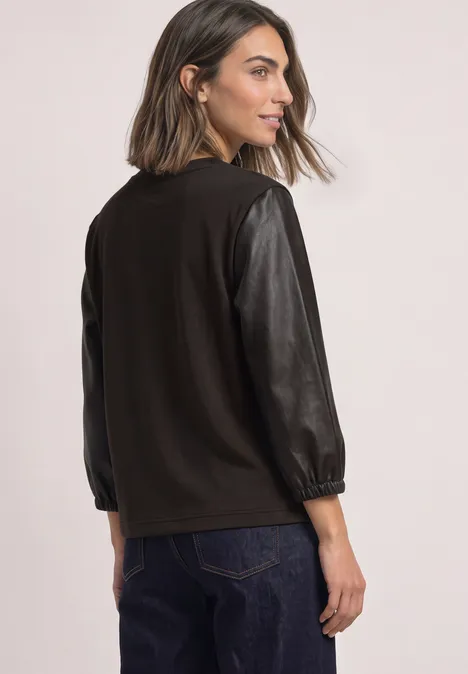 Shirt mit 3/4-Ärmeln in Leder-Optik black coffee Frau steht seitlich, trägt schwarzen Pullover mit Lederärmeln, blickt nach links.