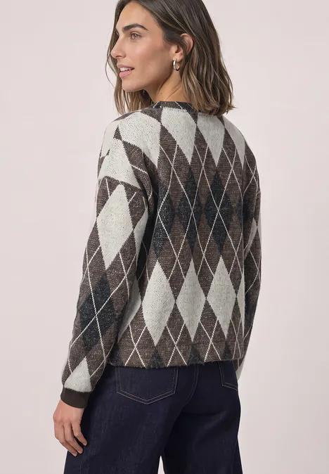 Jasje met ruitpatroon black coffee Frau mit brünettem Haar trägt argyle Strickpullover und Jeans, blickt seitlich über die Schulter.