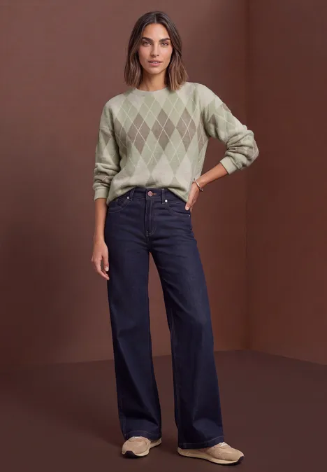 Shirt met lange mouwen, ronde hals en ruitjespatroon eucalyptus green Vrouw in groene ruittrui, wijde jeans en lichte loafers voor een bruine achtergrond.