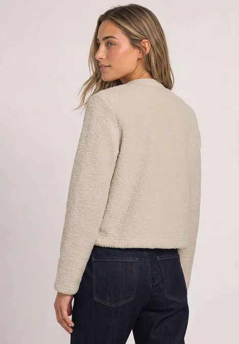 Teddyjasje met structuurdetails clay sand Een vrouw draagt een beige teddyjas en donkere jeans, ze kijkt over haar schouder.