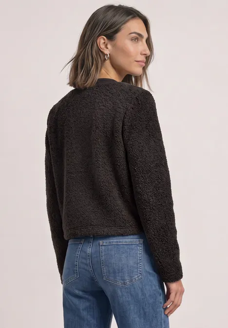 Teddyjasje met structuurdetails black coffee Vrouw van achter in zwarte teddyfleecejas en blauwe jeans, kijkt naar rechts.
