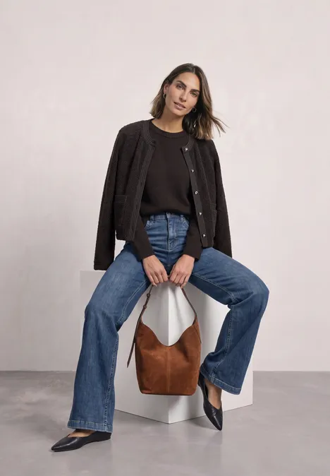 Teddyjasje met structuurdetails black coffee Vrouw zit op een wit blok, draagt zwarte cardigan, wijde jeans, zwarte schoenen en een bruine tas.