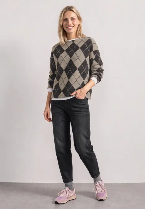 Langarm Shirt mit Turtle Neck und Muster clay sand Frau steht lächelnd im karierten Pullover, schwarzen Jeans und rosa Sneakern vor einem neutralen Hintergrund.