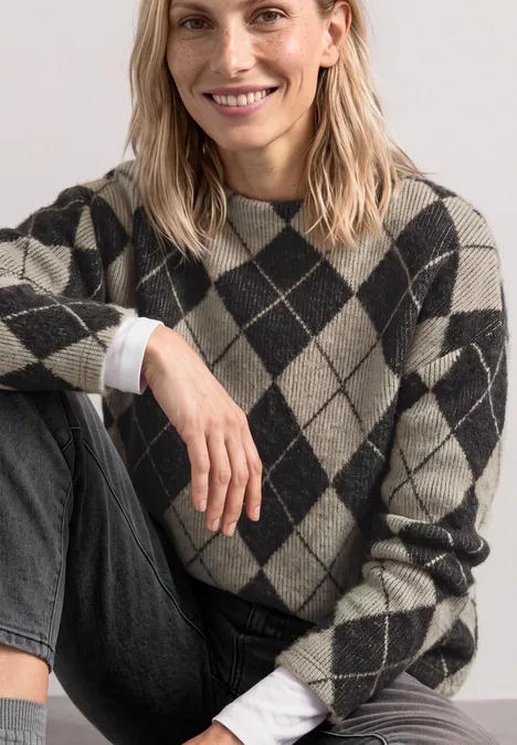 Langarm Shirt mit Turtle Neck und Muster clay sand Eine lächelnde Frau sitzt in Jeans und trägt einen karierten Pullover mit Rautenmuster.